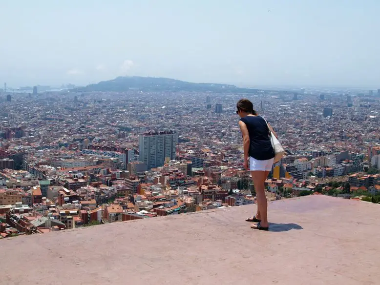 Mujer parada en la altura de una terraza abierta mirando hacia abajo la ciudad con temor al espacio abierto.
