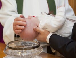 Persona sosteniendo a bebé que recibe del sacerdote el agua del bautismo, como signo de una convicción religiosa.