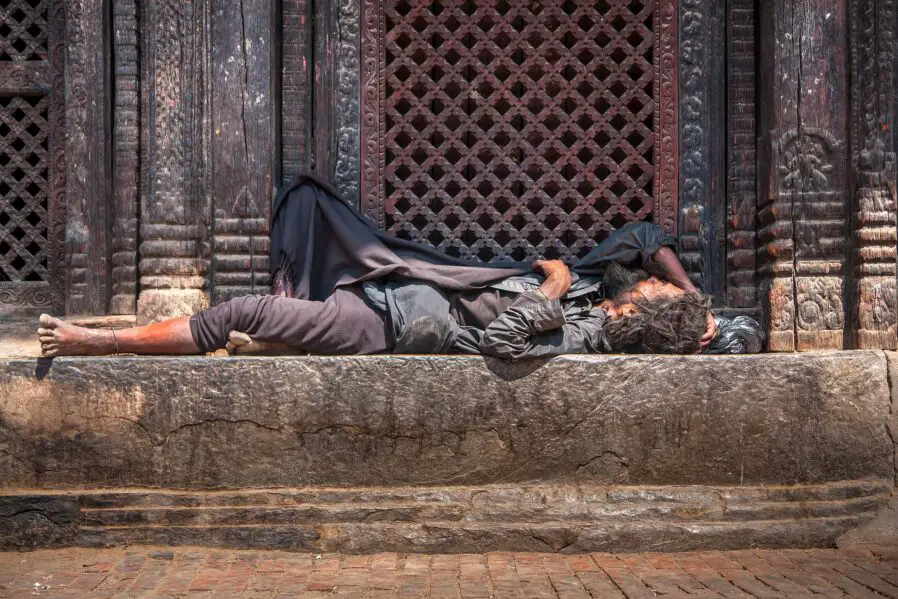 Persona marginal, sin hogar, durmiendo en la calle, frente a un portal.