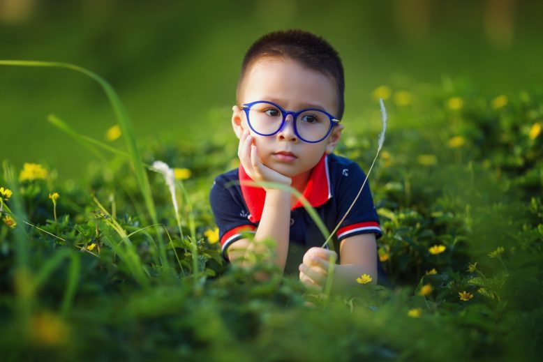 niño con anteojos acostado en el pasto, con mirada perspicaz