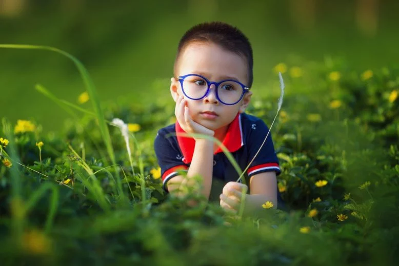 niño con anteojos acostado en el pasto, con mirada perspicaz