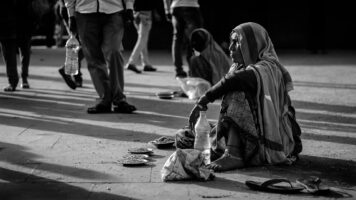 Mendigo sentado en peatonal, refleja necesidad de pensamiento complejo para resolver crisis sociales