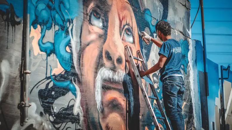 artista callejero sobre escalera pintando obra de arte urbano