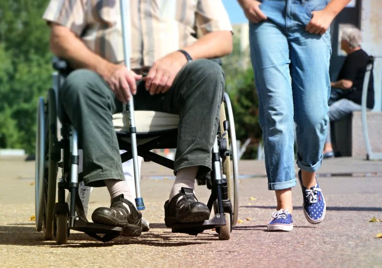 hombre en silla de ruedas con bastón para ciegos y persona cercana a ayudarlo por amor al prójimo